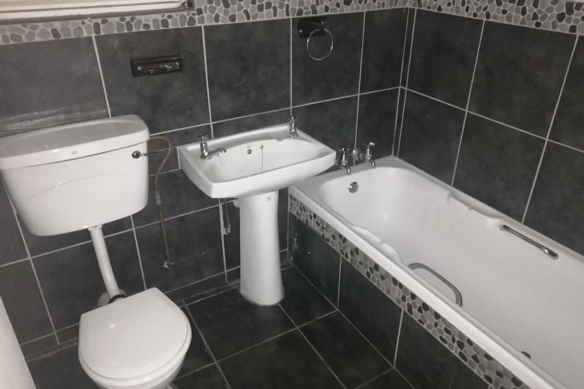 A functional bathroom featuring a pedestal washbasin, toilet, and bathtub with dark tiled walls and flooring.