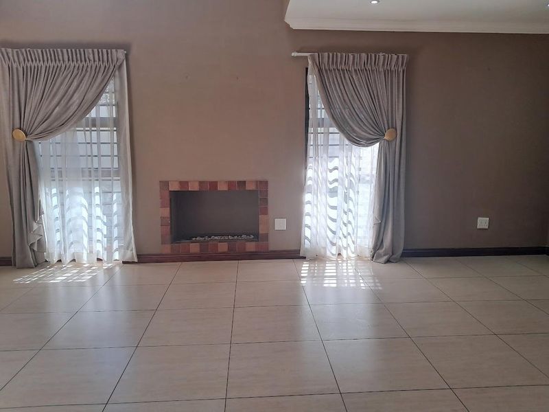 Spacious living room featuring neutral tiled flooring, a built-in fireplace with brick surround, and large windows with integrated curtain tracks.