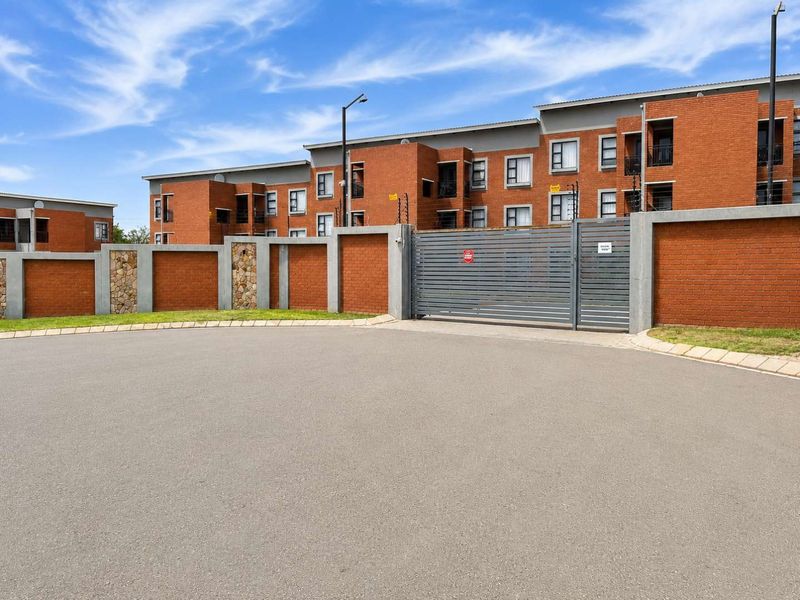 Front view of a modern apartment complex featuring a secure gated entrance, brick facade, and perimeter wall with electric fencing.