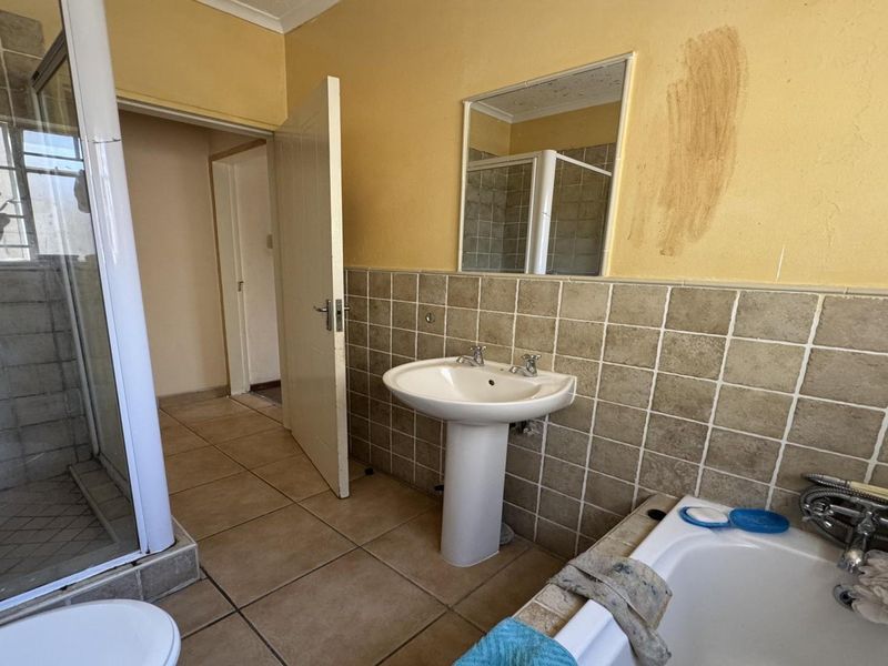 A dated bathroom featuring a pedestal basin, shower enclosure, and built-in bathtub with tiled finishes, requiring cosmetic updates to improve its overall condition.