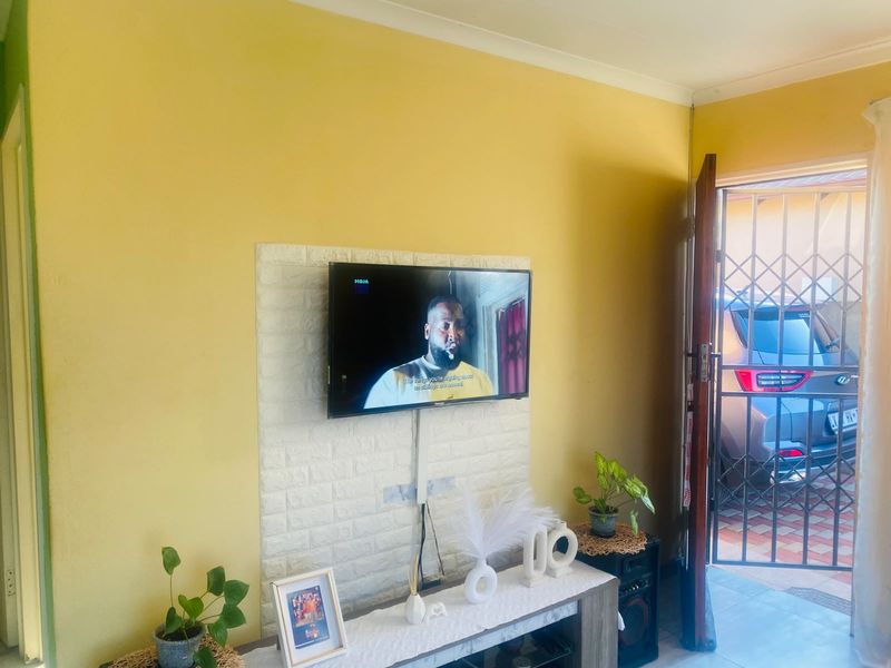 A living room featuring a textured feature wall with a mounted television and direct access to an exterior area through a security gate.