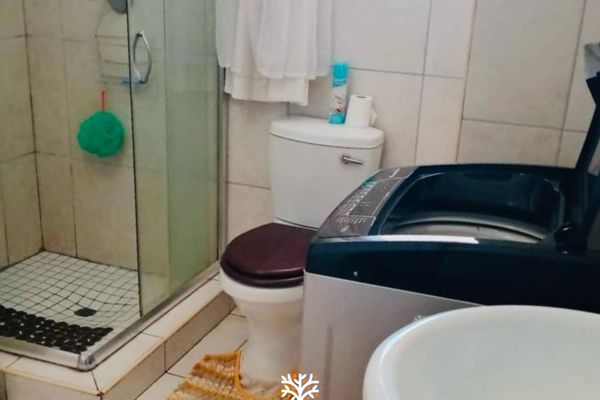 Compact bathroom featuring a glass-enclosed shower, standard toilet, and integrated laundry space with tiled finishes.