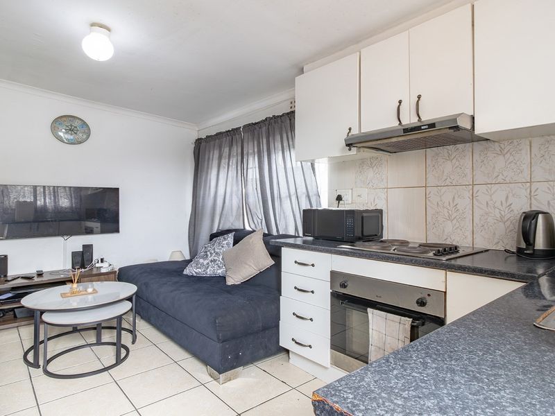 Compact open-plan living area featuring a functional kitchen with built-in cabinetry, electric hob, oven, and tiled flooring throughout the space.