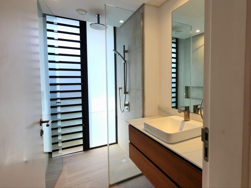 Modern bathroom featuring a floating vanity with a vessel sink, a walk-in shower with a rainfall showerhead, and floor-to-ceiling louvered windows.