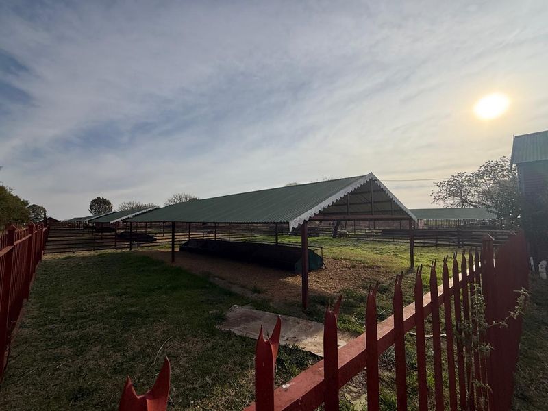 Outdoor farm utility area featuring covered livestock shelters with metal roofing and secure perimeter fencing.