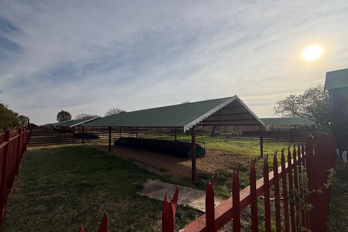 Outdoor farm utility area featuring covered livestock shelters with metal roofing and secure perimeter fencing.