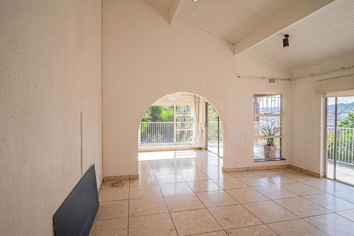 Spacious living area featuring vaulted ceilings with exposed beams, tiled flooring, and an arched transition leading to a balcony with scenic views.