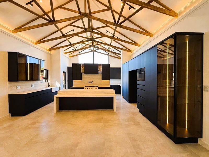 Modern, high-end kitchen featuring dark cabinetry, stone countertops, a central island, and striking exposed timber roof trusses with integrated lighting.
