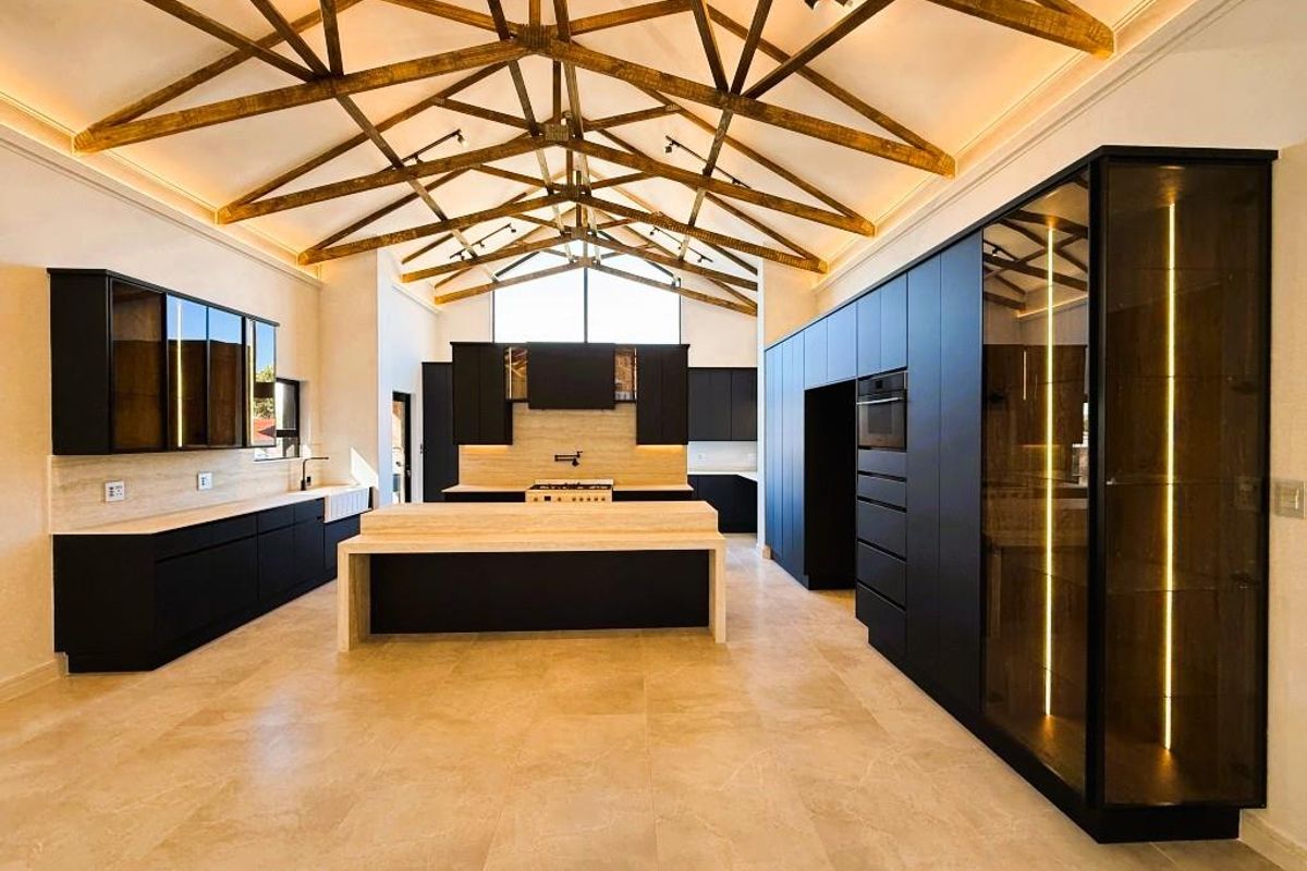 Modern, high-end kitchen featuring dark cabinetry, stone countertops, a central island, and striking exposed timber roof trusses with integrated lighting.