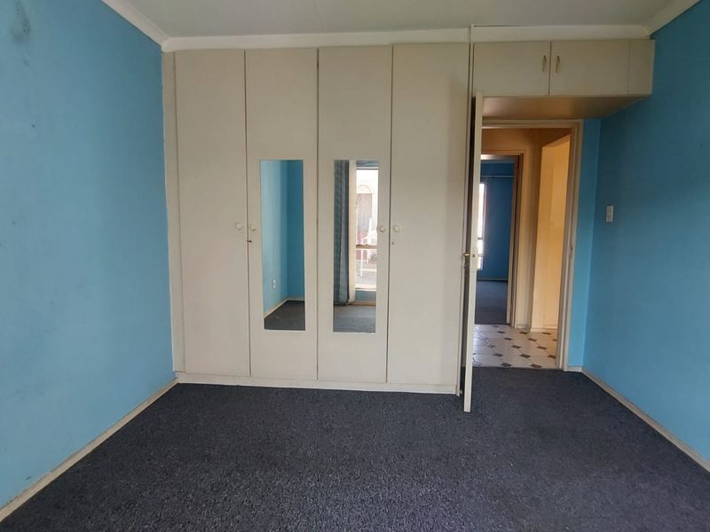 Empty bedroom featuring built-in cupboards with mirrored doors and carpeted flooring, requiring cosmetic updates to the walls and finishes.