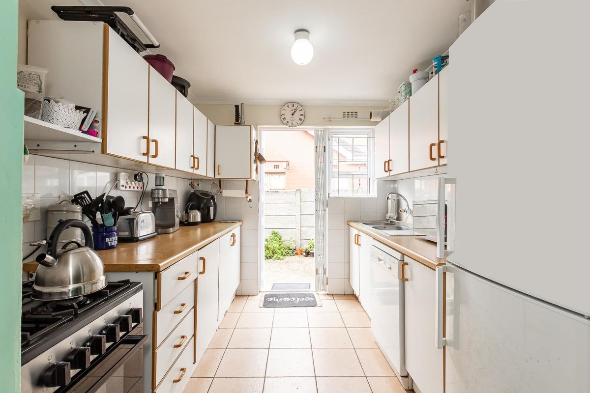 A functional galley-style kitchen featuring white cabinetry, wood-look countertops, tiled flooring, and direct access to the rear exterior.