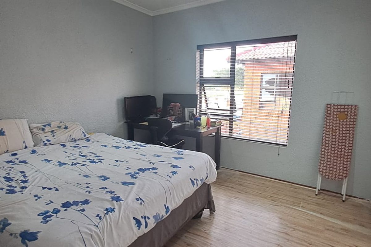 A bedroom featuring built-in cupboards, light-toned laminate flooring, and a window with fitted blinds.