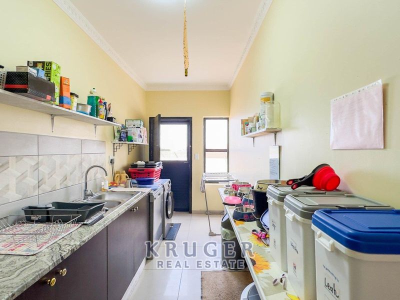 A functional laundry room featuring granite countertops, a stainless steel sink, built-in cabinetry, and tiled flooring with direct access to the exterior.