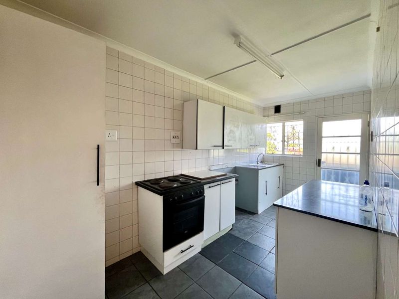 A functional kitchen featuring built-in cabinetry, an electric stove, and tiled finishes. The space is vacant and ready for modernization.