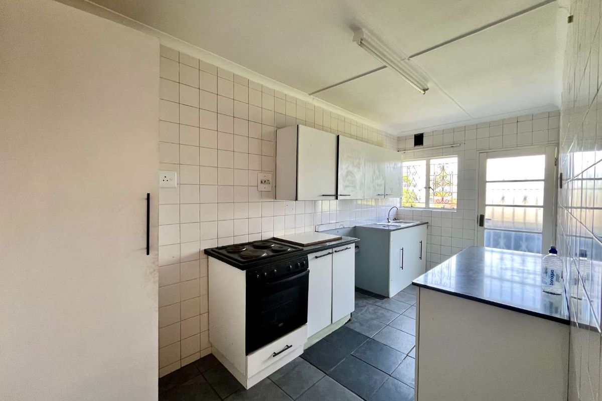 A functional kitchen featuring built-in cabinetry, an electric stove, and tiled finishes. The space is vacant and ready for modernization.