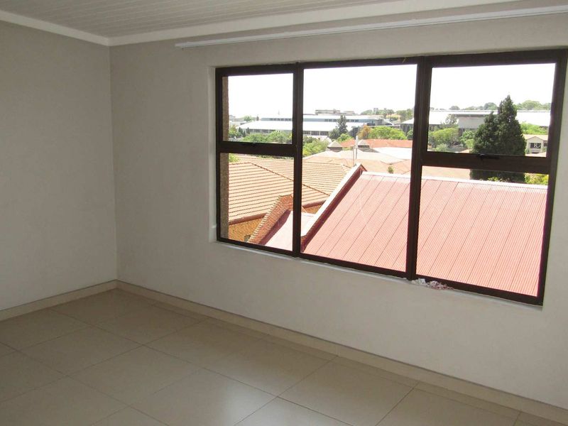 An empty bedroom featuring neutral tiled flooring, clean walls, and large aluminium-framed windows providing natural light and an elevated view.
