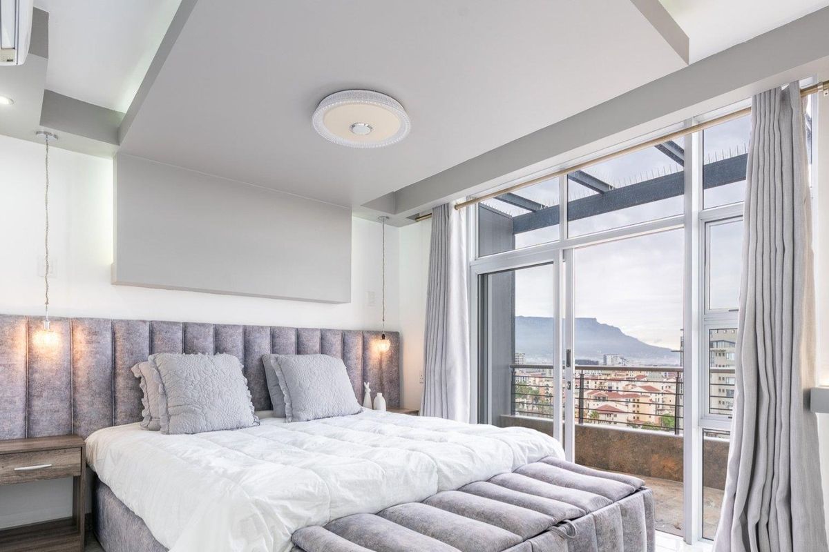 Modern bedroom featuring a built-in headboard, recessed ceiling lighting, and large sliding glass doors opening onto a balcony with scenic city and mountain views.