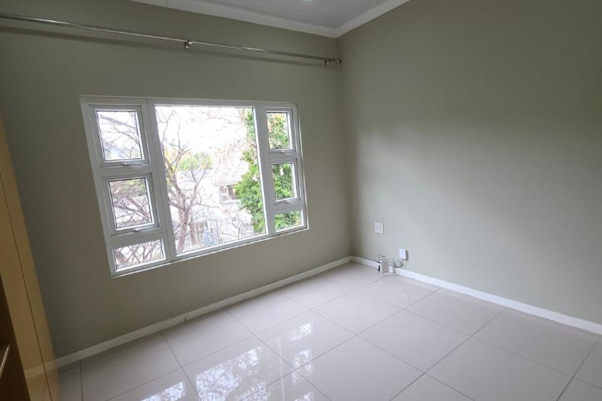 A bright, empty bedroom featuring neutral wall tones, large windows, recessed ceiling lighting, and polished floor tiles.