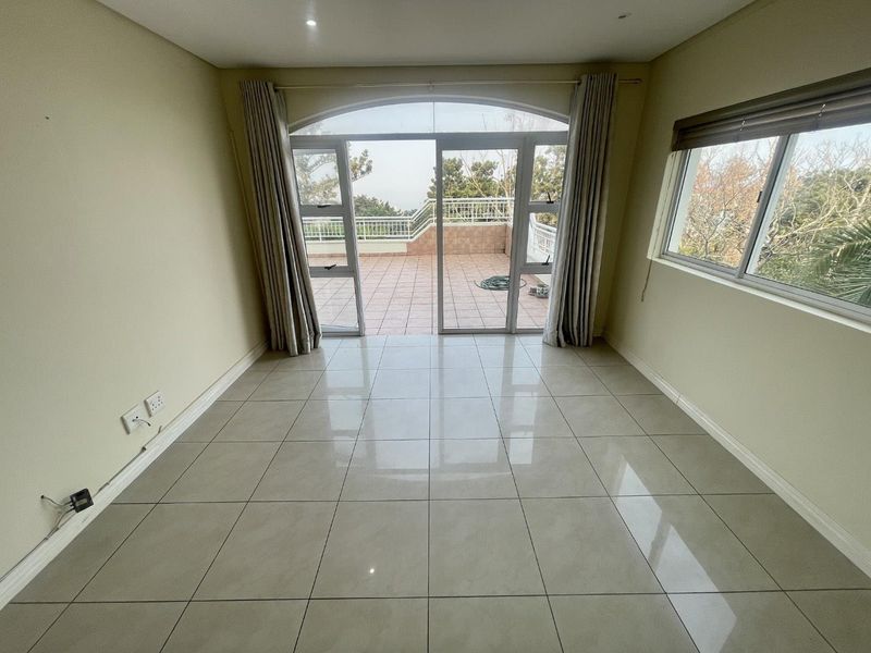 An empty, light-filled living room featuring large tiled floors and sliding glass doors that open onto a spacious outdoor balcony.