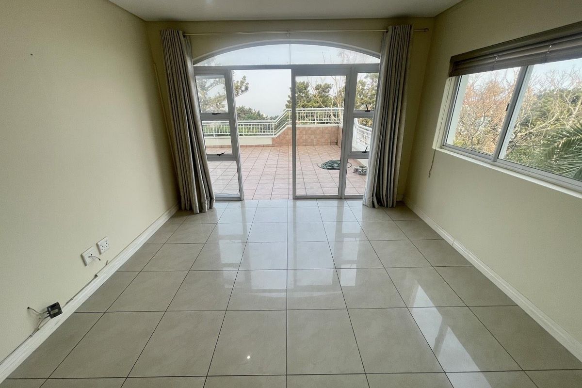 An empty, light-filled living room featuring large tiled floors and sliding glass doors that open onto a spacious outdoor balcony.