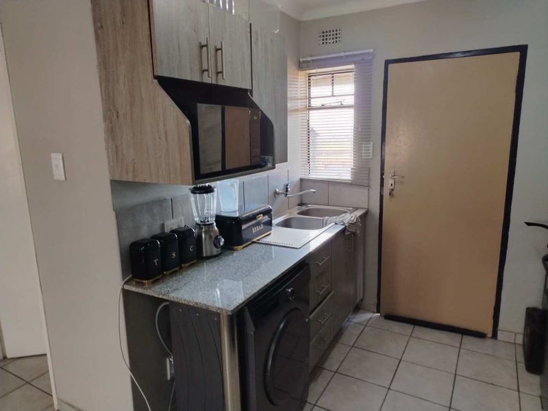 Compact kitchen featuring granite countertops, built-in cabinetry, a stainless steel double sink, and tiled flooring with a functional layout.
