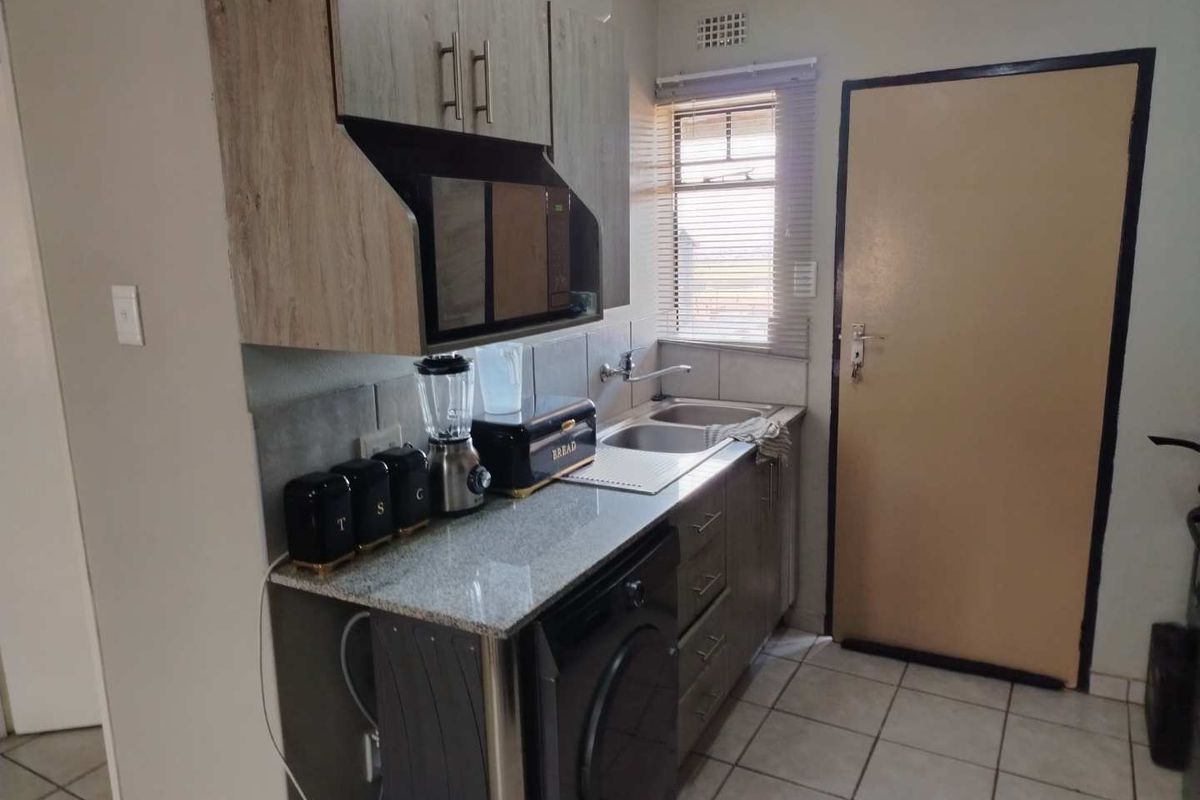 Compact kitchen featuring granite countertops, built-in cabinetry, a stainless steel double sink, and tiled flooring with a functional layout.