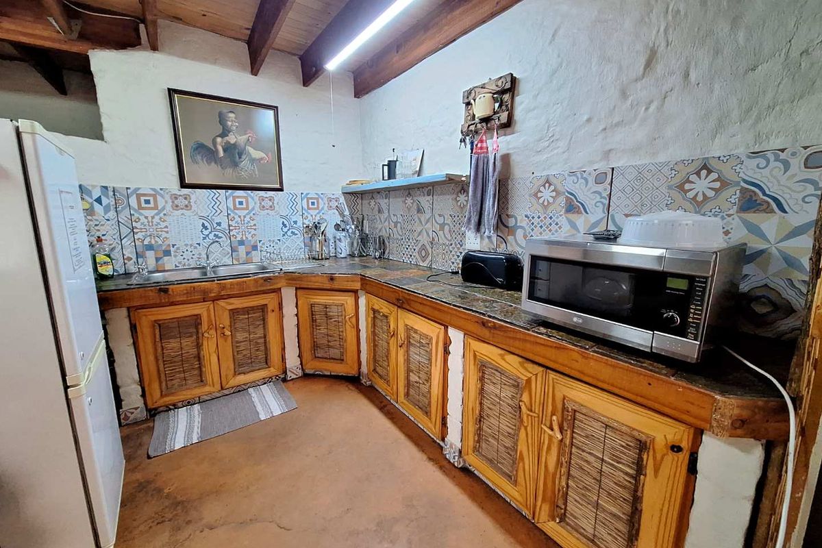 Rustic kitchen featuring wooden cabinetry, patterned tile backsplash, exposed timber ceiling beams, and a double basin sink.