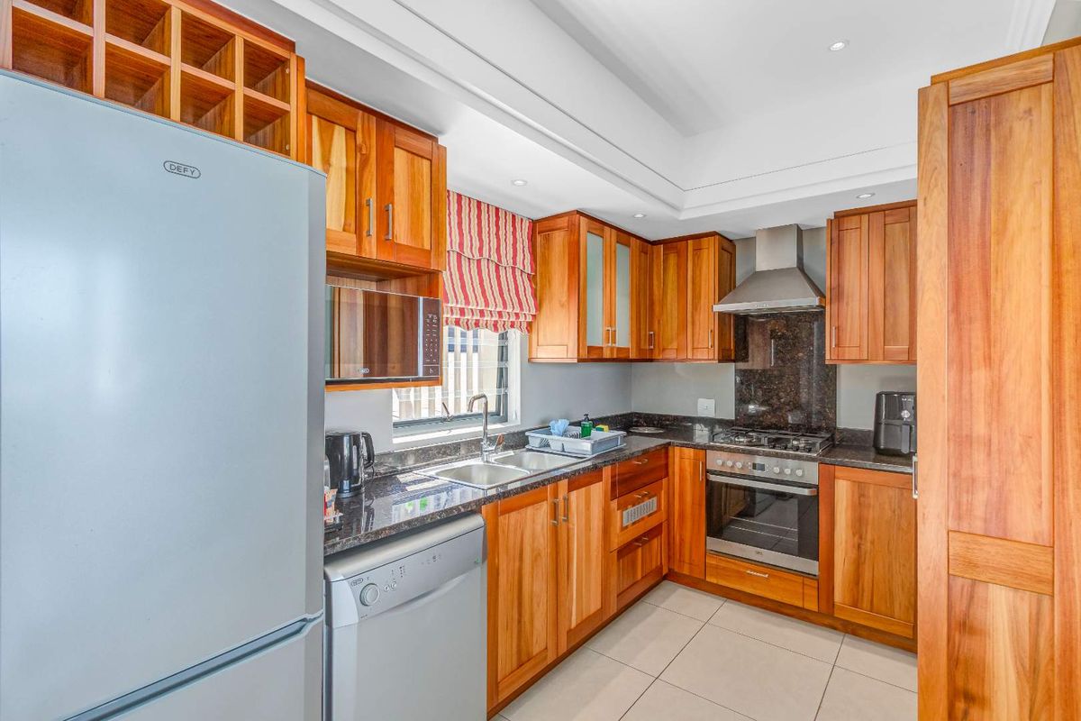 A well-maintained kitchen featuring warm timber cabinetry, granite countertops, a stainless steel gas hob, extractor fan, and built-in oven.