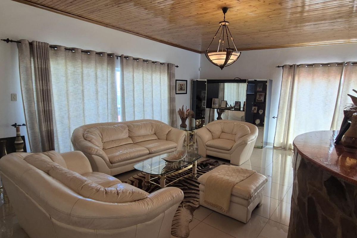 Spacious living room featuring a warm timber tongue and groove ceiling, tiled flooring, and a built-in bar area with feature stone cladding.