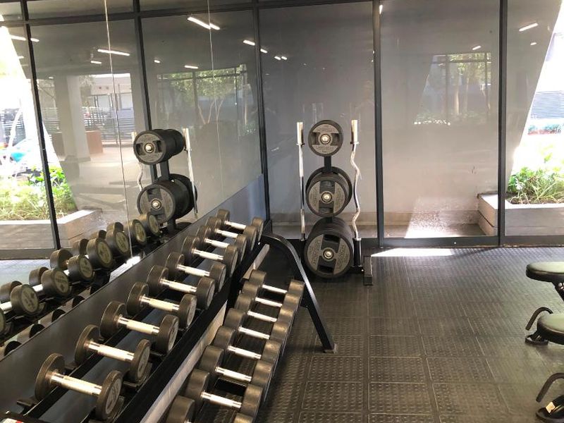 A well-maintained apartment gym featuring durable rubber flooring, full-length wall mirrors, and floor-to-ceiling glass partitions providing a bright, modern workout environment.