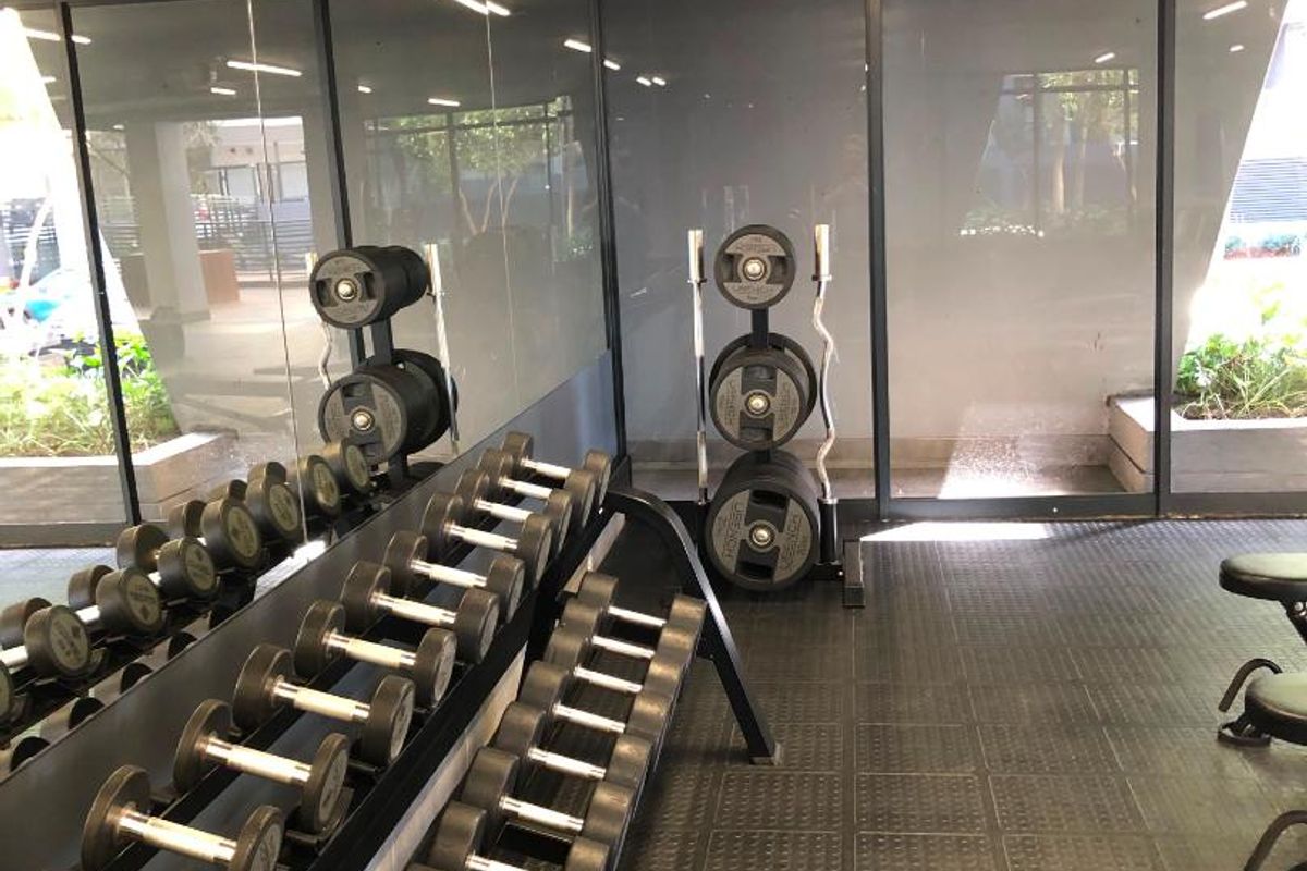 A well-maintained apartment gym featuring durable rubber flooring, full-length wall mirrors, and floor-to-ceiling glass partitions providing a bright, modern workout environment.