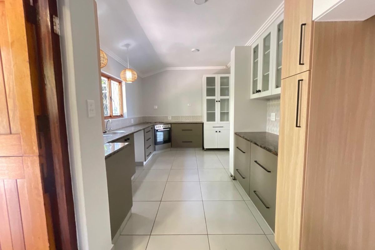 A spacious, modern kitchen featuring neutral-toned cabinetry, stone countertops, built-in oven, and tiled flooring, offering a clean and functional layout.