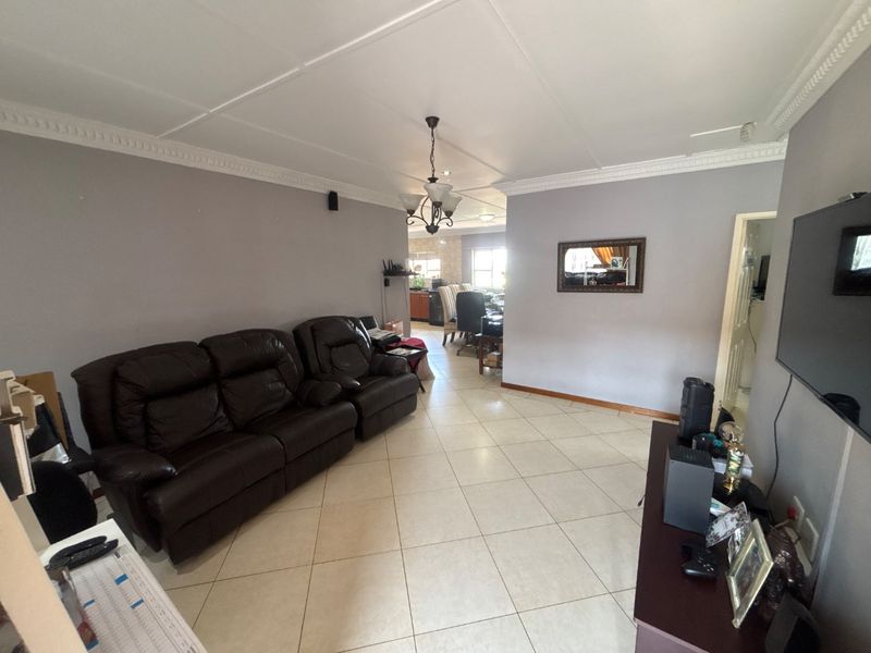 Open plan living area featuring neutral wall tones, tiled flooring, and decorative ceiling cornicing, providing a functional space that flows into the adjacent dining area.