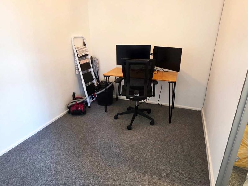 A compact office space featuring grey carpet flooring and neutral walls, suitable for a dedicated workspace or small study area.