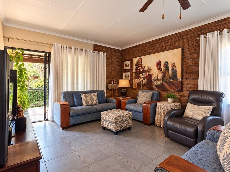 A comfortable living room featuring an exposed brick feature wall, tiled flooring, and direct access to an outdoor patio area through sliding glass doors.