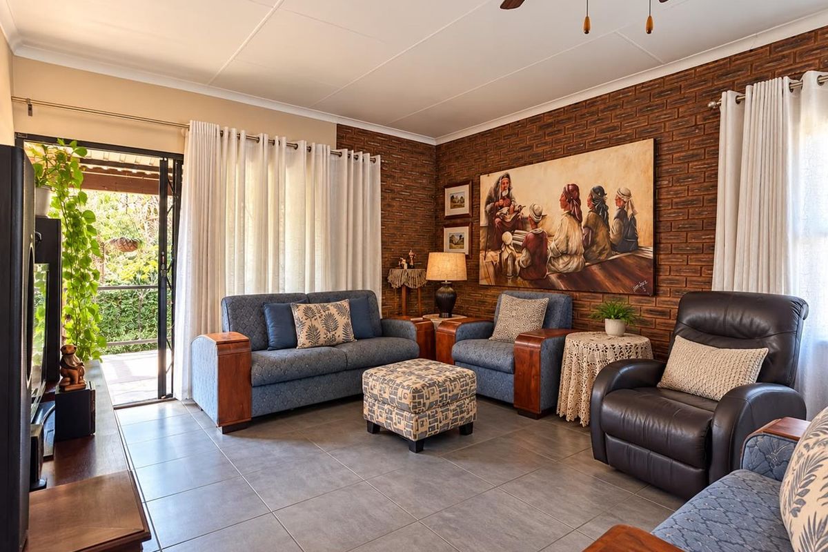 A comfortable living room featuring an exposed brick feature wall, tiled flooring, and direct access to an outdoor patio area through sliding glass doors.