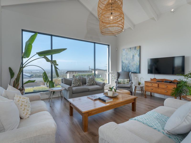 Bright and spacious living room featuring vaulted ceilings with exposed beams, large floor-to-ceiling windows, and modern laminate flooring with scenic views.