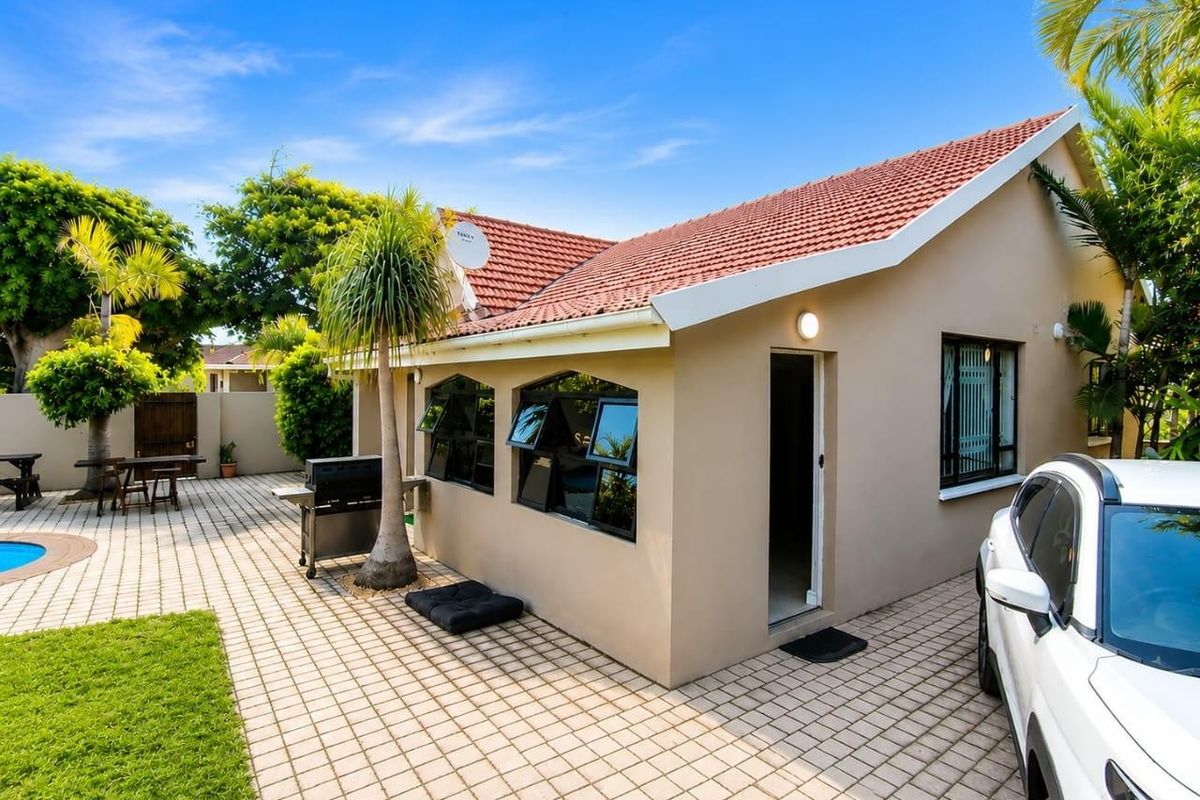 Rear exterior view of the house featuring a paved patio area, swimming pool, and well-maintained garden surroundings.