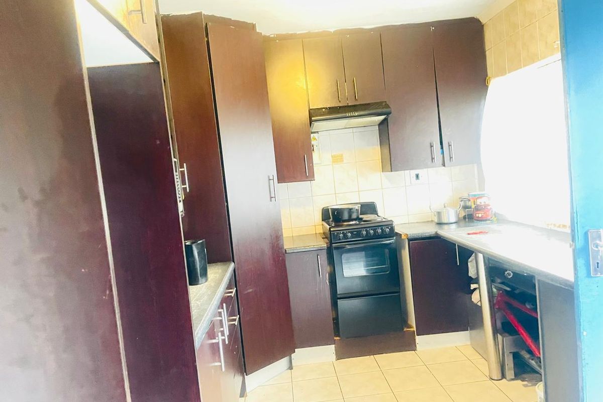 A compact kitchen featuring dark wood-finish cabinetry, tiled flooring, a tiled backsplash, and a freestanding oven with an integrated extractor fan.