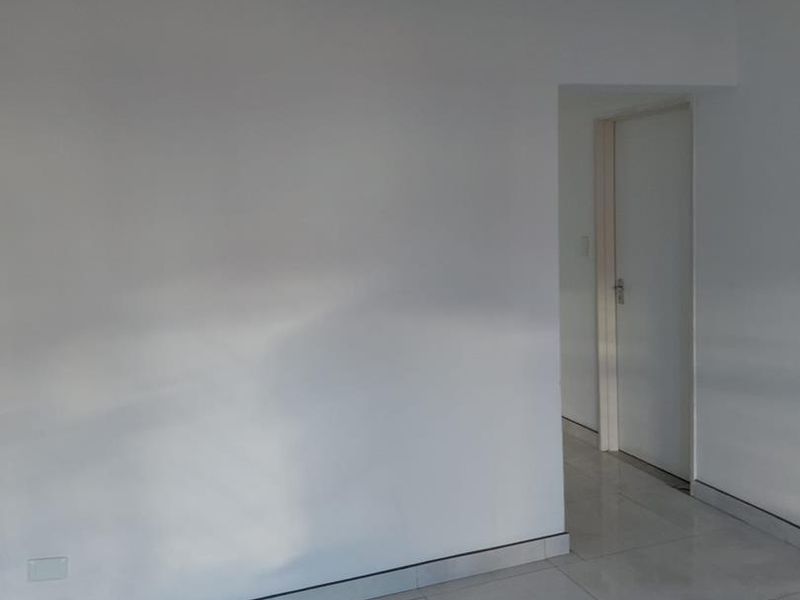 An empty living area featuring neutral tiled flooring and clean white walls, leading to an internal doorway.