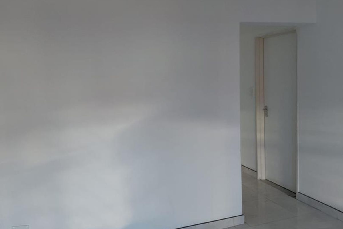 An empty living area featuring neutral tiled flooring and clean white walls, leading to an internal doorway.