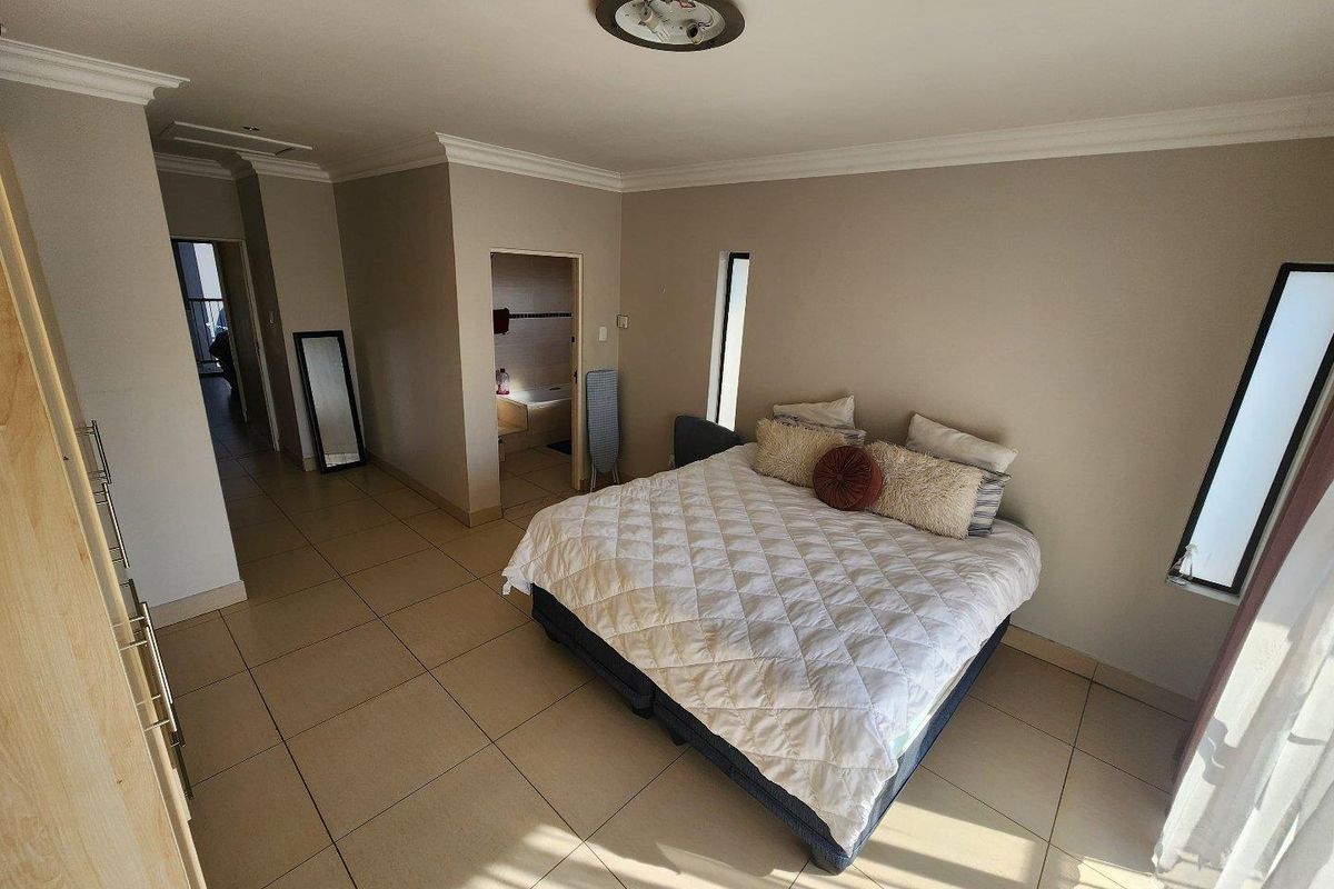 Spacious bedroom featuring neutral tiled flooring, en-suite bathroom access, and vertical windows providing natural light.
