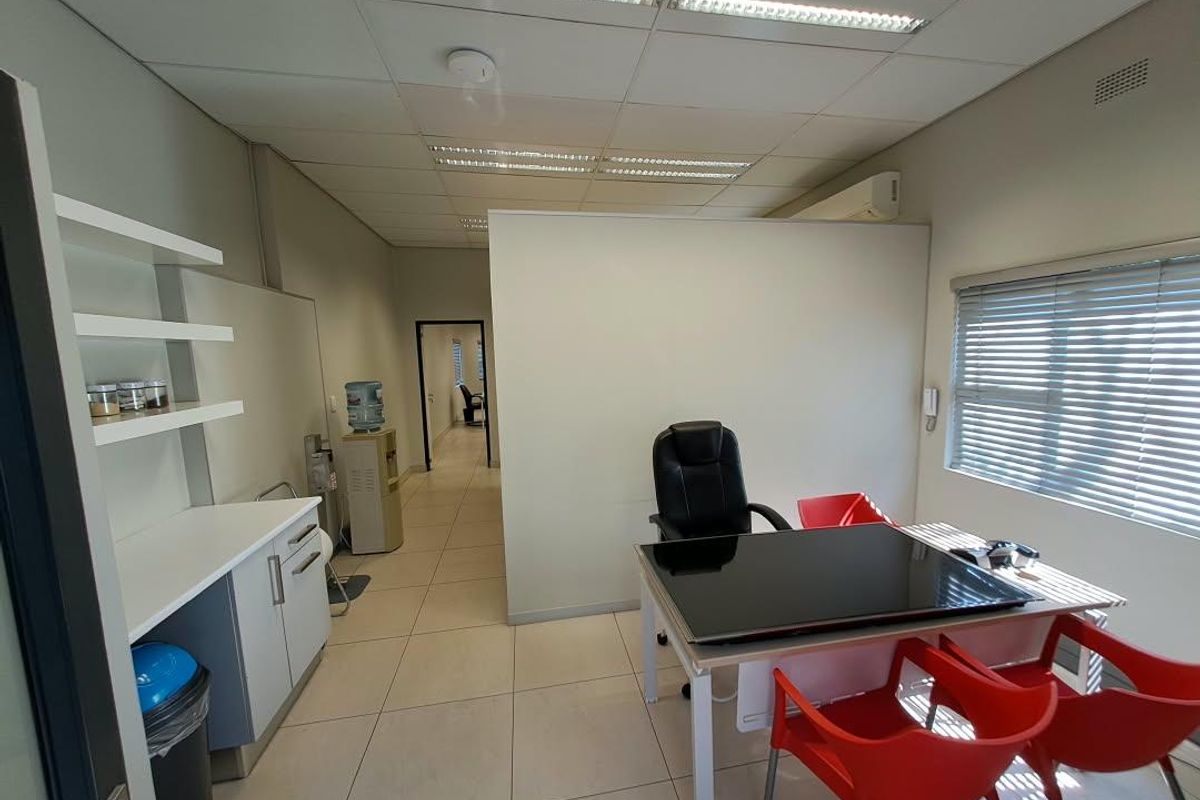 A functional office space featuring tiled flooring, a suspended ceiling with recessed lighting, a small kitchenette area, and an integrated air conditioning unit.
