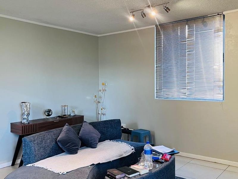 A living room featuring tiled flooring, track lighting, and a window fitted with venetian blinds.