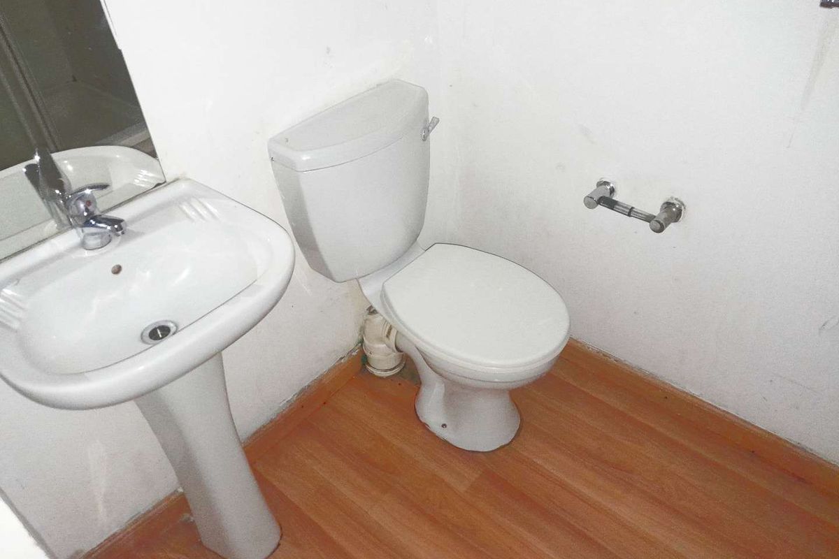 A compact bathroom featuring a pedestal basin and toilet with laminate flooring, requiring minor cosmetic updates to improve the overall finish.