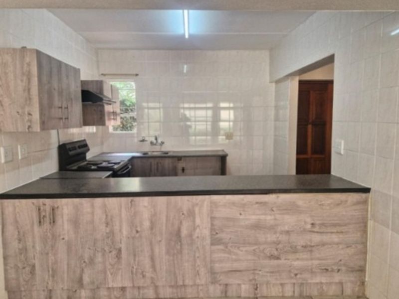A functional kitchen featuring wood-look laminate cabinetry, dark countertops, a stainless steel sink, and a built-in extractor fan with tiled wall finishes.
