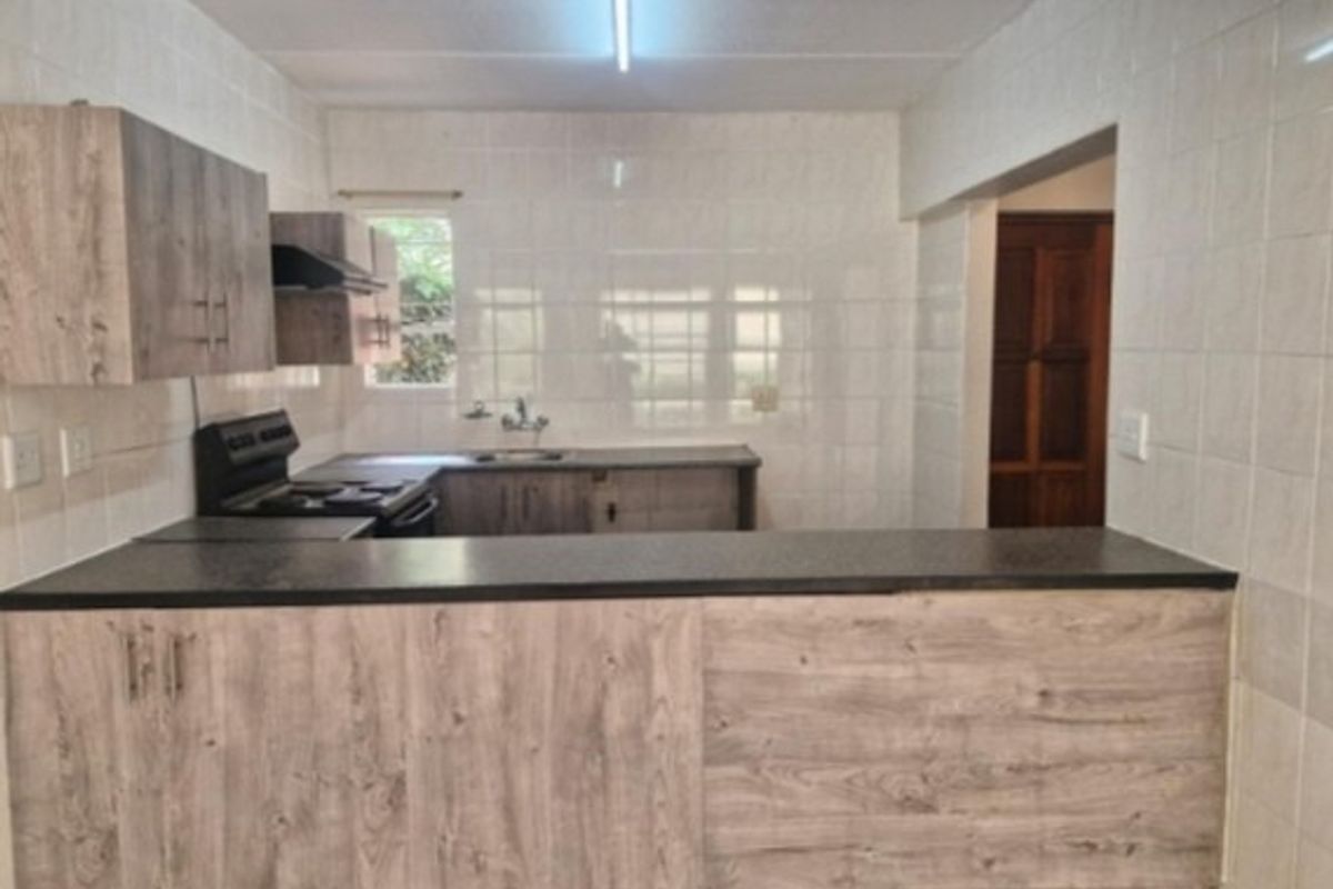 A functional kitchen featuring wood-look laminate cabinetry, dark countertops, a stainless steel sink, and a built-in extractor fan with tiled wall finishes.