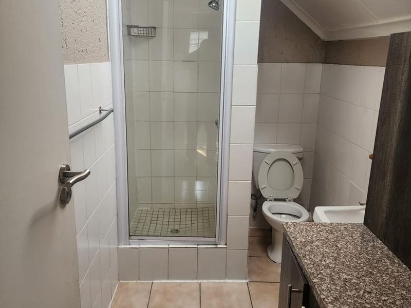 Compact bathroom featuring a shower enclosure, toilet, vanity with granite countertop, and a skylight providing natural light.