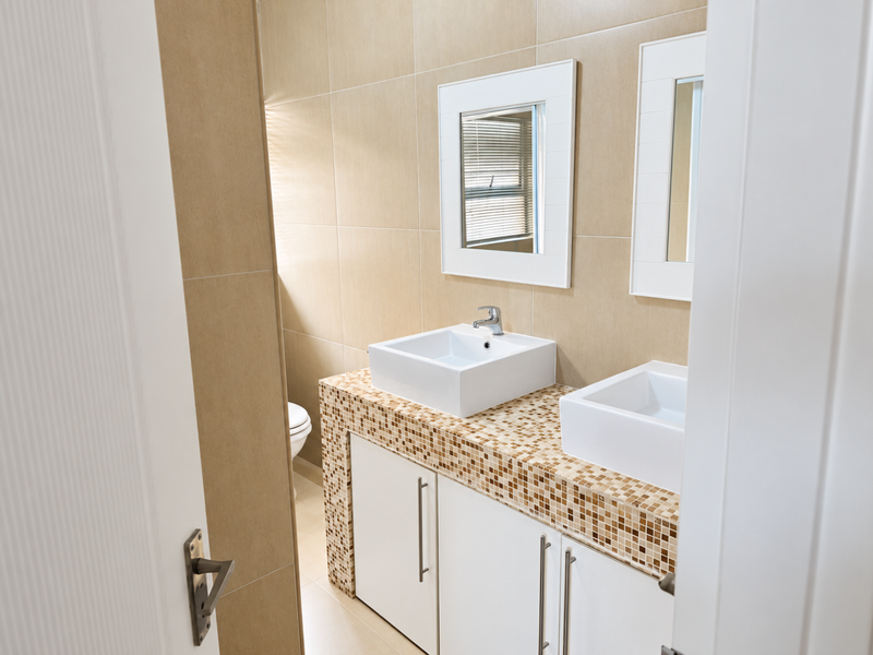 Modern bathroom featuring a double vanity with vessel sinks, mosaic tile countertop, and wall-mounted mirrors, finished with neutral wall tiling.