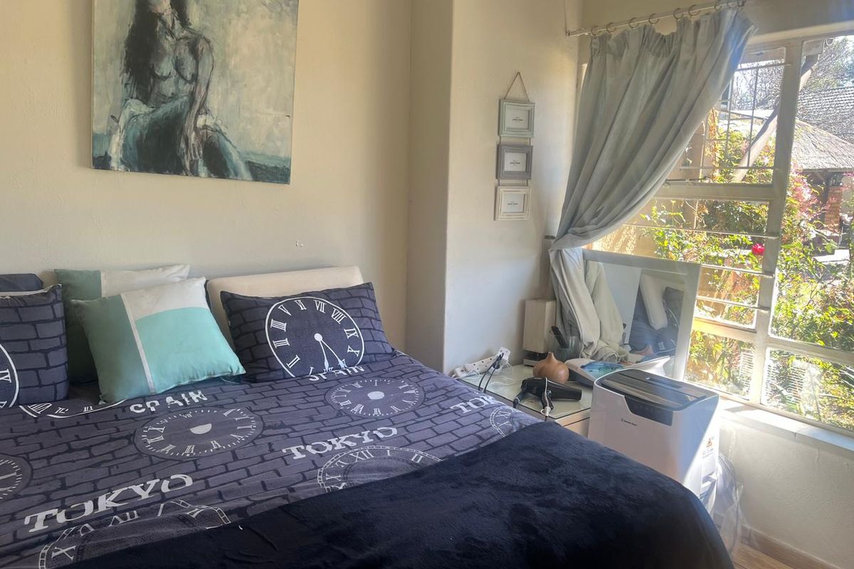 A bedroom featuring laminate flooring and a large steel-framed window allowing natural light into the space.